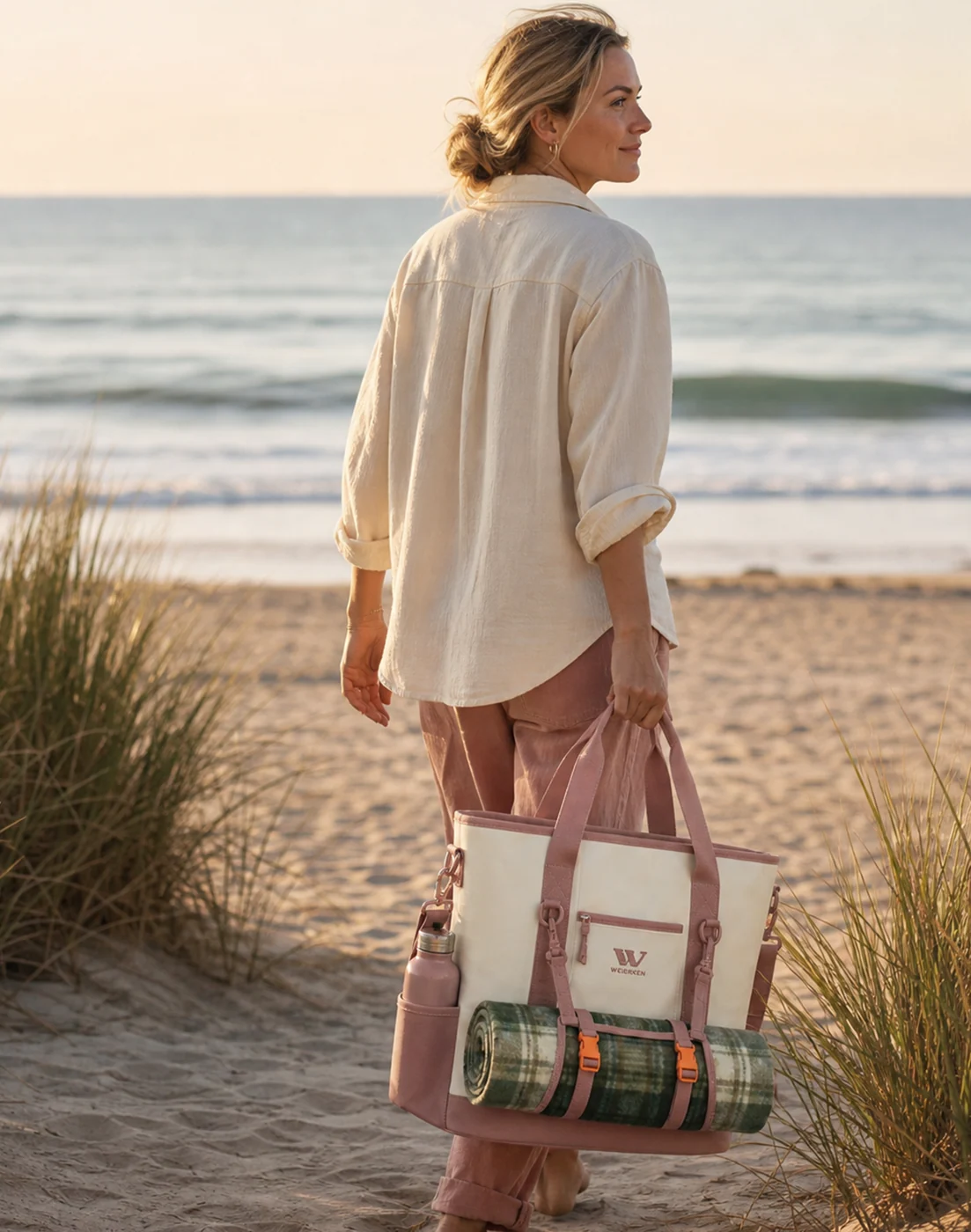 Woman carrying a tote with a blanket and water bottle on a beach path